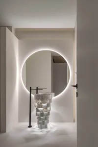A minimalist bathroom with a modern marble sink and a circular mirror illuminated from behind.