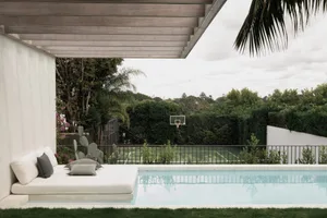 A modern outdoor living space featuring a concrete patio with a plush seating area, a tranquil pool, and lush greenery.