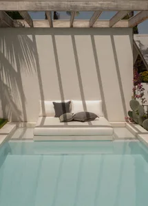 A modern poolside lounge with concrete flooring and a wooden pergola structure.