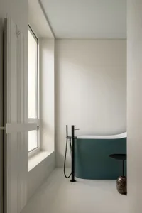 A minimalist bathroom featuring a modern concrete bathtub and a window allowing natural light to enter.