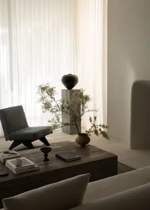 A minimalist living room featuring a wooden coffee table, a modern grey chair, and a vase with flowers.