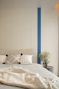 A minimalist white bedroom interior with a bed, white pillows, and a blue accent stripe on a white wall.