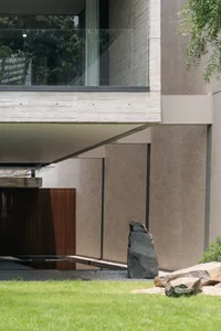 Modern house with concrete walls, glass window, and stone sculpture in the garden.