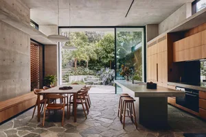 A modern kitchen featuring concrete and glass materials with a stone floor and large windows looking out to a garden.