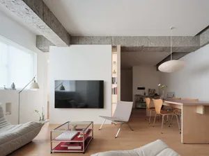 Modern living room with minimalist design, featuring wooden flooring, white walls, and a sleek glass coffee table.