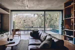 A modern living room featuring a concrete ceiling, a leather sofa, a wooden coffee table, and a bookshelf filled with books a