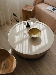 A modern living room featuring a round wooden table with a ceramic bowl and a metal sculpture.