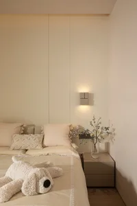 A minimalist bedroom decorated with neutral-toned textiles, featuring a cozy stuffed animal on the bed and a vase of flowers