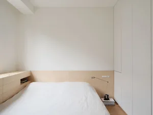 Minimalist bedroom with a white platform bed, wood floor, and white walls.
