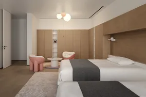 Modern minimalist bedroom with wooden walls and built-in cabinets, featuring a pink accent chair and table, and a comfortable