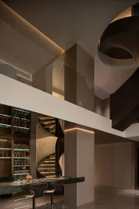 A sleek, modern reception area with a glass staircase, black leather stools, and a contemporary bar.