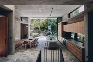 Modern residential kitchen featuring a concrete floor, wooden cabinets, and a large window overlooking a garden.