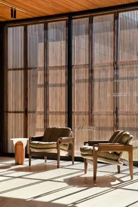 Two brown leather armchairs with wooden legs and cushions, placed in a room with large wood-paneled windows and a wooden floo