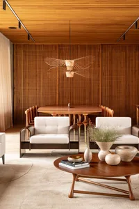 A modern living room with wooden walls, flooring, and furniture, featuring a round dining table, two white armchairs, and a c