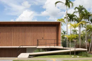 Modern library exterior made of wood with a ramp and palm trees.