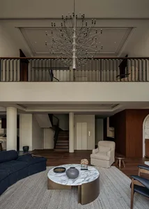 A modern living room with a marble coffee table, black couch, and beige armchair.