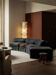 A modern living room featuring a comfortable sofa, a unique floor lamp, and a wooden stool. The space is adorned with a natur