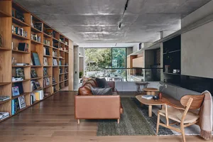 L-shaped brown leather sofa, wooden coffee tables, and bookshelves filled with books in a modern living room.