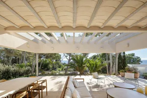 Modern minimalist outdoor living space with white lounge furniture, wooden table, and greenery.