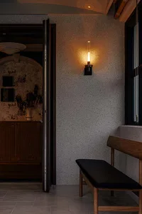A modern residential hallway featuring a concrete textured wall, wooden bench, and warm lighting from a wall-mounted fixture.
