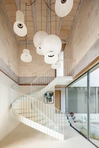Modern residential interior featuring a spiral staircase adorned with hanging paper lanterns, complemented by a concrete ceil
