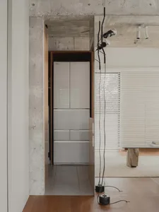 A minimalist kitchen with concrete walls, a tall, sleek refrigerator, and modern lighting fixtures.