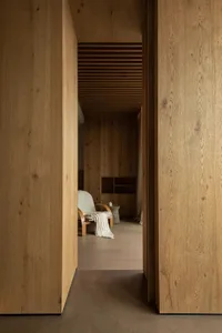 A minimalist interior with wooden walls, a light green armchair, and a small table with a cup.