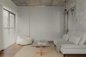 Seating area featuring modern minimalist design with concrete walls, glass table, and fabric furniture.