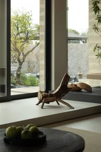 A minimalist wooden window sill with a natural, textured finish, featuring a small wooden sculpture and a collection of green