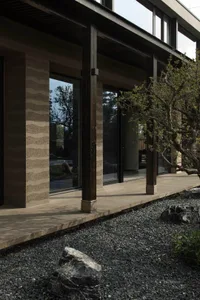 Modern house exterior with concrete and wooden columns and a gravel garden with rocks and plants.