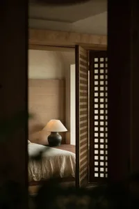 Minimalist bedroom featuring natural wood elements, with a cozy atmosphere created by a lit table lamp and a comfortable bed.