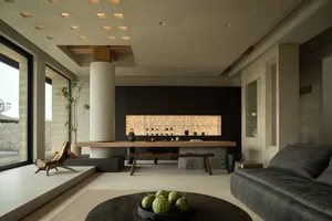 Modern living room with exposed concrete ceiling and walls, featuring a large table with vases and potted plants.