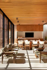 Modern living room with wooden walls and floors, white furniture, and a flat-screen TV.