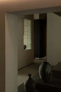 Modern living room with concrete walls and floor, featuring a large vase and a glass display case.