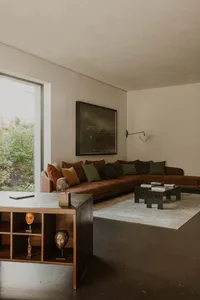 A modern living room with a brown sectional sofa, green and brown throw pillows, and abstract art on the wall. Concrete floor