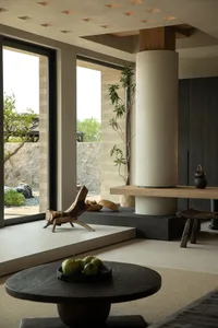 Modern living room with minimalist design, featuring wooden and concrete elements, and a round wooden table with green fruit 