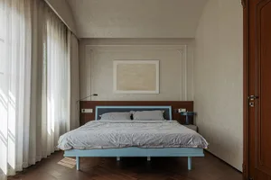 A minimalist bedroom featuring a blue bed, grey linens, and a simple white artwork on the wall.