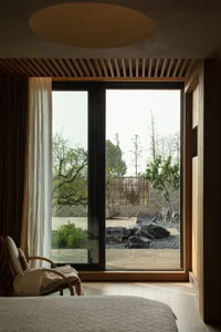 A modern minimalist bedroom with a large glass window overlooking a serene outdoor garden.