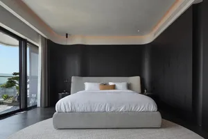 A modern minimalist bedroom featuring black walls, a white upholstered bed with a low-profile headboard, and a large window p