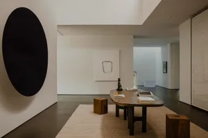 A modern minimalist space featuring a concrete floor, wooden table, and fabric rug with abstract art and minimal decor.