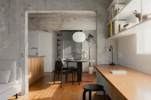 Minimalist residential space featuring concrete walls and floor, with a flat white table and chairs in the center.