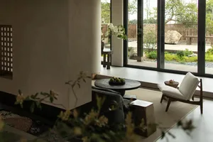 A minimalistic living room with concrete walls and a view of a garden.