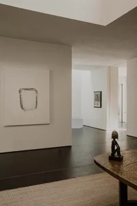 A minimalistic industrial interior with concrete flooring and walls, featuring a wooden table with a metallic base and a scul