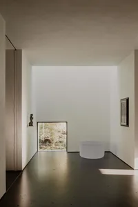 A minimalist interior designed with concrete surfaces, featuring a small window and a round white object on the floor.