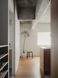 A minimalist kitchen with concrete ceiling beams, wooden flooring, and a small potted plant in the corner.