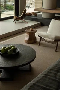 A modern minimalist living room with wooden furniture and decor, featuring a round black table with green melons, a white cus