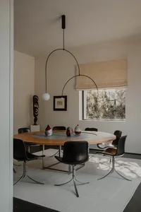 A modern dining room featuring a round wooden table with a metal base, black chairs, and a minimalist design.