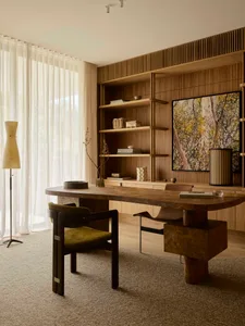 A modern home office featuring a wooden desk and shelving unit with decorative items and a large artwork.