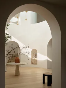 Modern minimalist interior space with light-colored walls, arched doorways, and natural light.