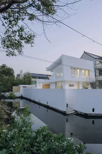 一座現代白色住宅外觀，搭配玻璃窗，坐落於寧靜水域旁，營造出平和安詳的氛圍。